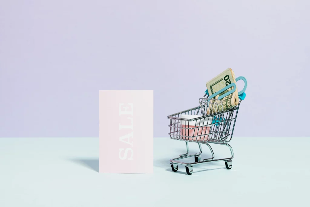 A mini shopping cart with money in it, next to a 'SALE' sign